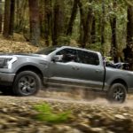 A grey 2022 Ford F-150 Lightning is shown from the side off-roading in the woods after winning a 2022 Ford F-150 Lightning vs 2022 Tesla Cybertruck comparison.