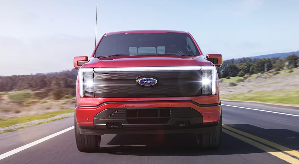 A red 2022 Ford F-150 Lightning is shown from the front driving on an open road.