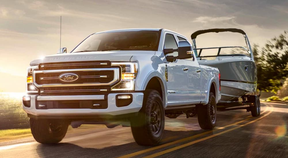 A white 2022 Ford F-350 Lariat is showing towing a boat on a highway.