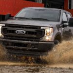A brown 2022 Ford F-350 XL is shown driving through a mud puddle during a 2022 Ford F-350 vs 2022 Chevy Silverado 3500 HD comparison.