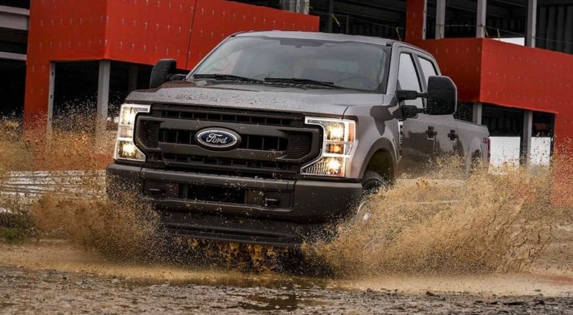A brown 2022 Ford F-350 XL is shown driving through a mud puddle during a 2022 Ford F-350 vs 2022 Chevy Silverado 3500 HD comparison.