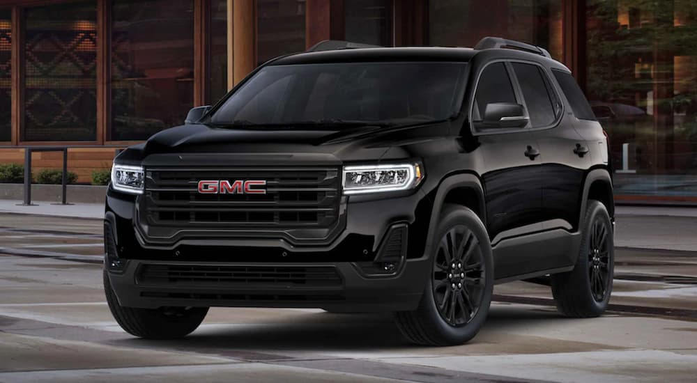 A black 2022 GMC Acadia is shown from the front parked in front of a modern building.