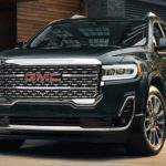 A black 2022 GMC Acadia is shown from the front parked in front of a modern building.