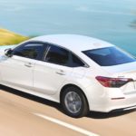 A white 2022 Honda Civic LX is shown driving past a lake.