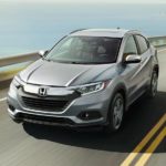 A silver 2022 Honda HR-V is shown driving along a ocean view highway.