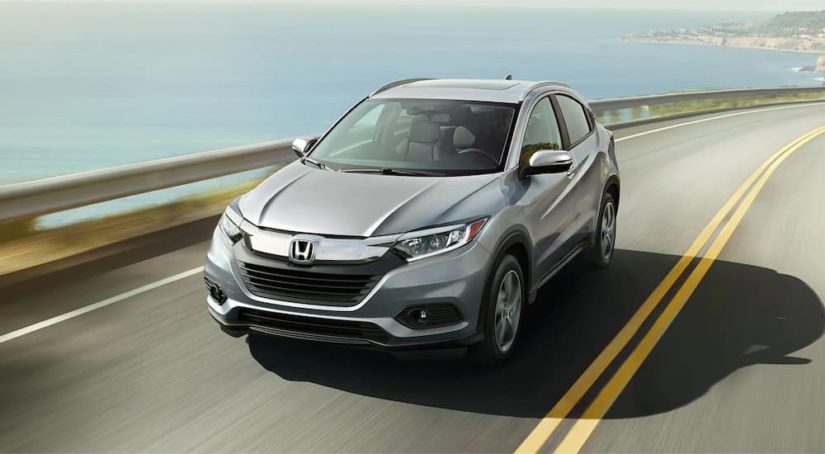 A silver 2022 Honda HR-V is shown driving along a ocean view highway.