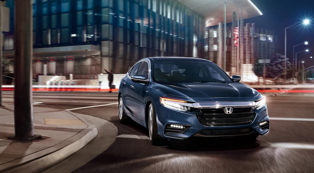 A blue 2022 Honda Insight Touring is shown driving in a city at night.