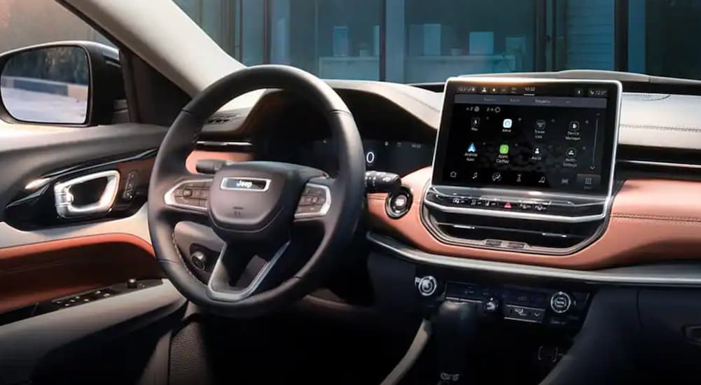 The black and brown interior of a 2022 Jeep Compass shows the steering wheel and infotainment screen.
