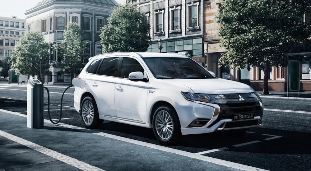 A white 2022 Mitsubishi Outlander PHEV is shown parked at an EV charging station.