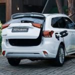 A couple is shown next to white 2022 Mitsubishi Outlander PHEV while it's charging in a driveway.