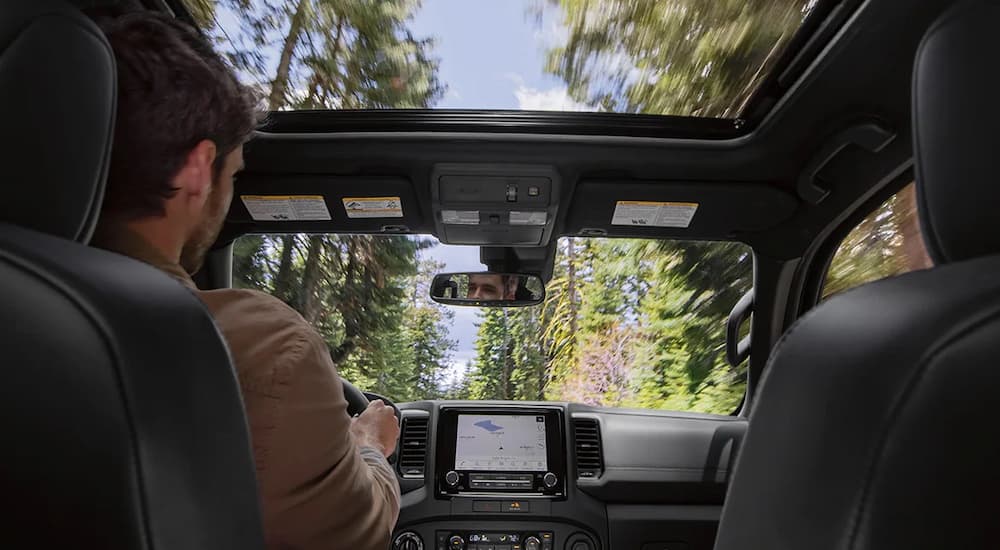 A close up of a man driving a 2022 Nissan Frontier shows the moonroof, front seats, and infotainment screen.