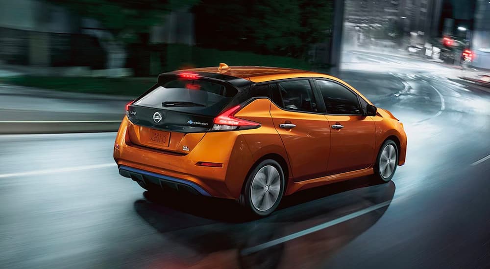 An orange 2022 Nissan LEAF is shown from the rear driving down a city road at night.