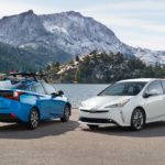 A blue 2022 Toyota Prius XLE is parked next to a white Limited in the mountains near a lake.