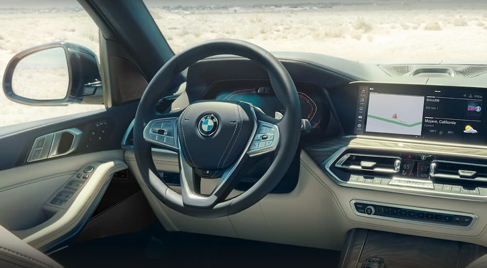 The black and white interior of a 2022 BMW X7 shows the steering wheel and infotainment screen.
