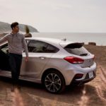A man is shown stepping out of his white 2019 Chevy Cruze by the beach.