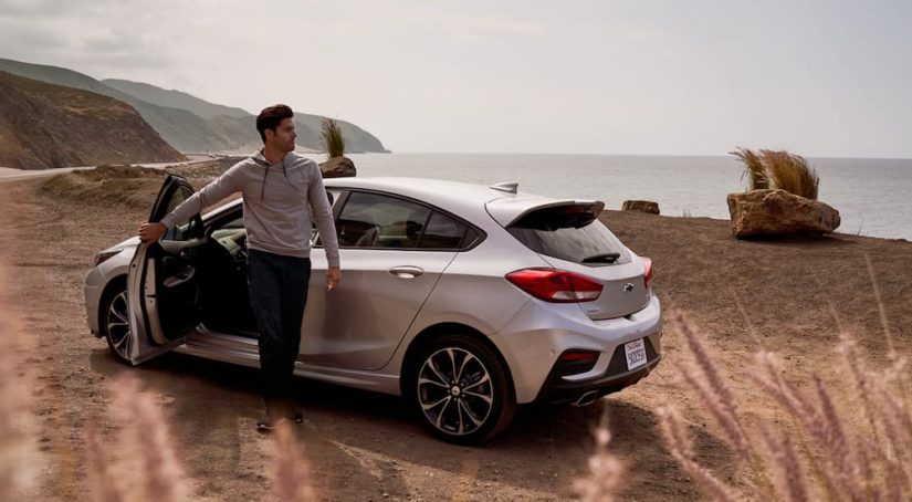 A man is shown stepping out of his white 2019 Chevy Cruze by the beach.