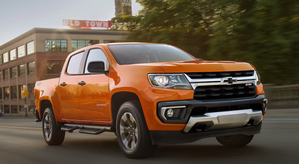 An orange 2021 chevy Colorado is shown from the side driving through a city after leaving a Chevy dealer.