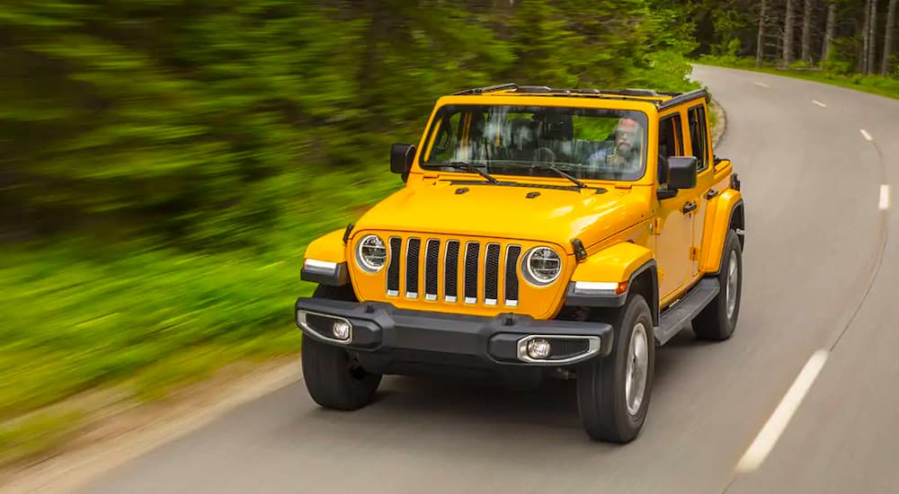 A yellow 2021 Jeep Wrangler Unlimited is shown driving past trees.