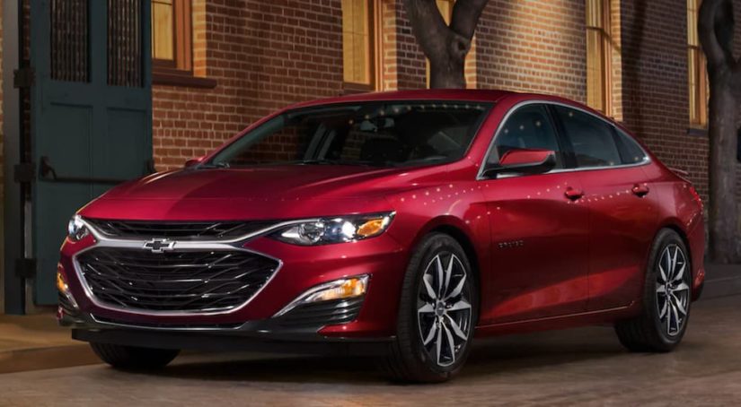 A red 2022 Chevy Malibu is shown from the front parked next to a brick building after researching GM lease turn in.