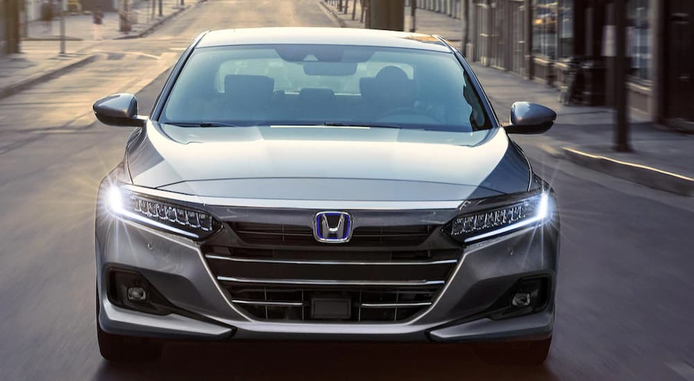A silver 2021 Honda Accord Hybrid is shown from the front driving through a city.
