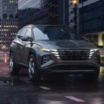 A grey 2022 Hyundai Tucson is shown driving on a city street at night.