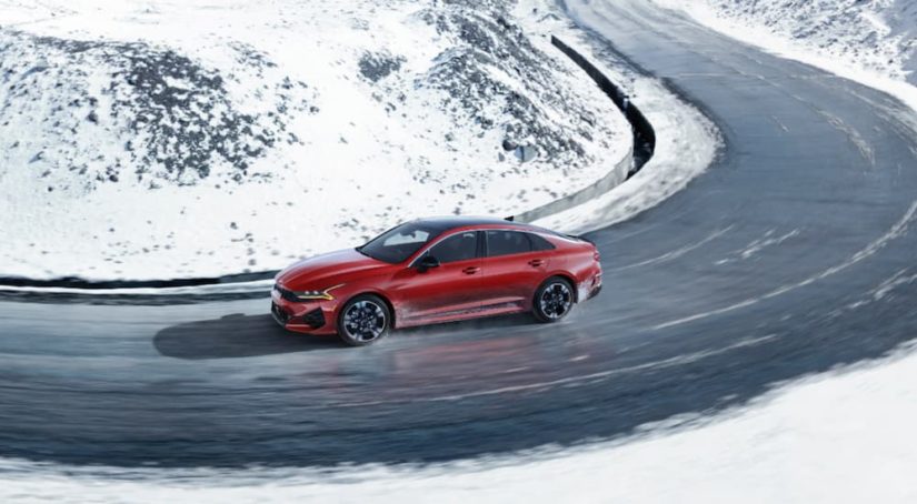 A red 2022 kia K5 is shown from the side driving on a snow lined road.