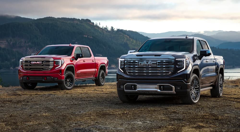 A red 2022 GMC 1500 Sierra AT4-X and a dark blue Denali Ultimate are shown parked by a lake.