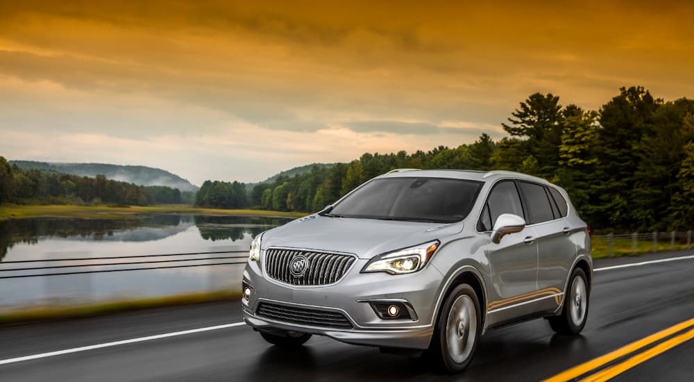 A 2018 used Buick Envision is shown driving next to a lake.