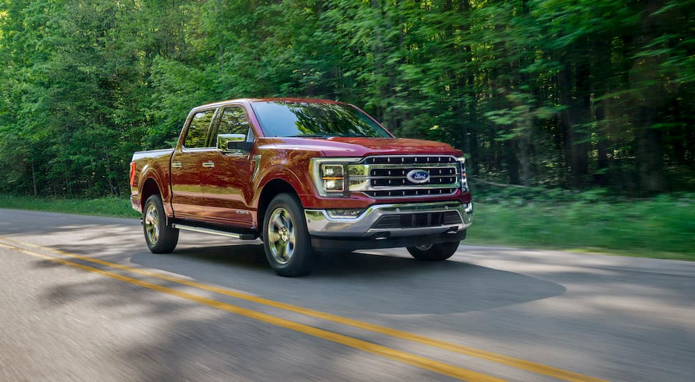 A red 2020 Ford F-150 Lariat is shown driving down a wooded road.