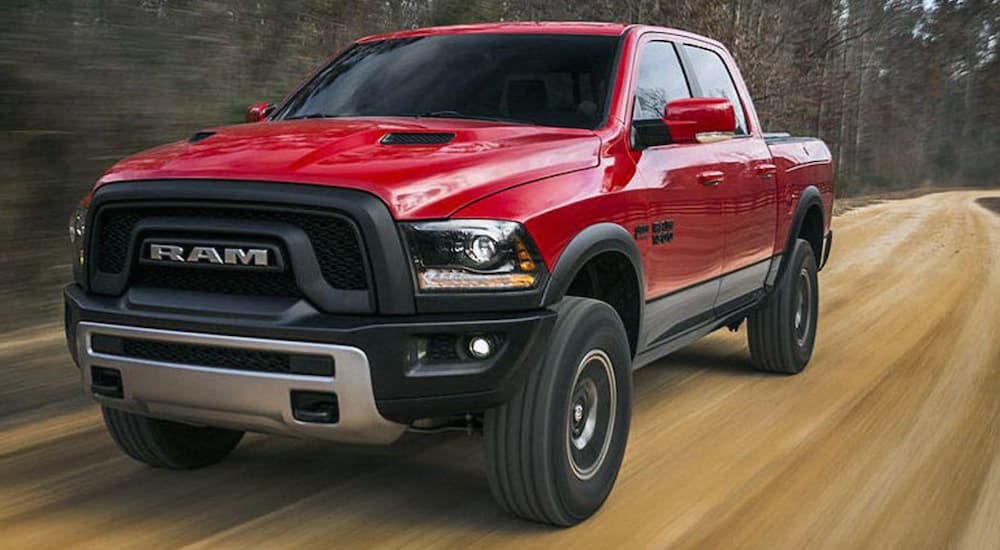 A side view of a red 2020 Ram 1500 Rebel is shown driving down a dirt road after leaving a used Ram dealer.