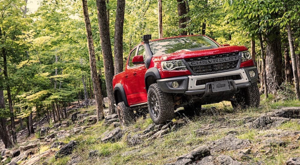 A red 2020 Chevy Colorado ZR2 is shown off-roading in the woods after leaving a used truck dealership.