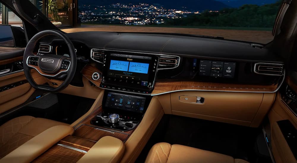 The tan and black leather interior of a 2022 Jeep Grand Wagoneer shows the steering wheel and center console.