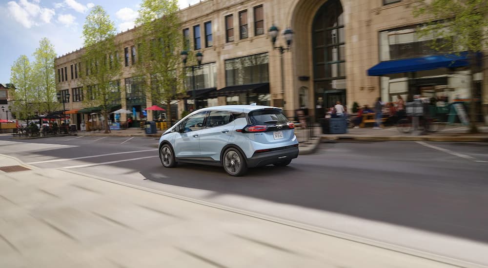 A light blue 2022 Chevy Bolt EV is shown driving past buildings in a city.