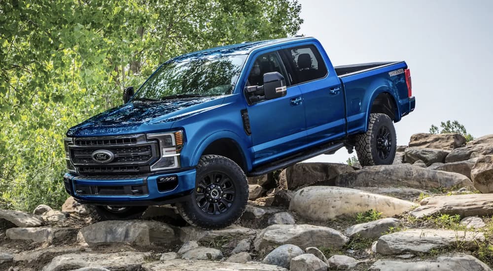 A blue 2022 Ford F-250 is shown from the side off-roading in the mountains. 