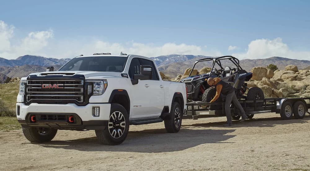 A white 2022 GMC Sierra 2500 HD is shown parked in the desert towing dune buggies on a trailer.