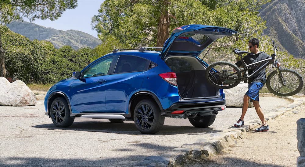 A man is shown putting a bicycle into the rear cargo space of a blue 2022 Honda HR-V Sport.