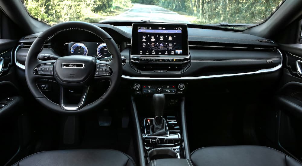 The black interior of a 2022 Jeep Compass shows the steering wheel and infotainment screen.
