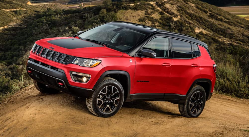 A red 2022 Jeep Compass Trailhawk is shown off-roading on a dirt trail.