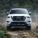 A white 2022 Nissan Armada is shown from the front off-roading in the forest.