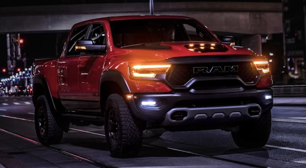 An orange 2022 Ram 1500 TRX is shown from the front driving through the city at night.