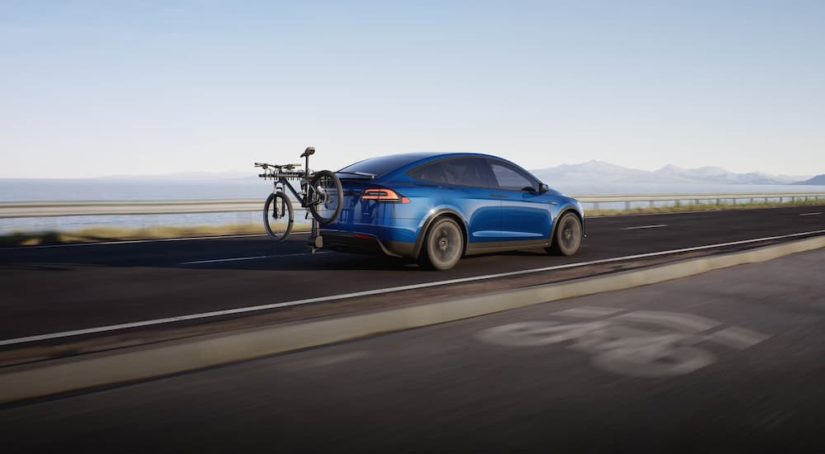 A blue 2022 Tesla Model X is shown from the rear with a bike mounted in the rear.