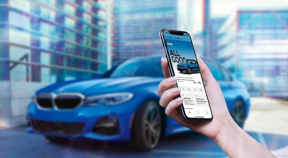 An arm holding a phone is shown in front of a blue BMW 3Series.