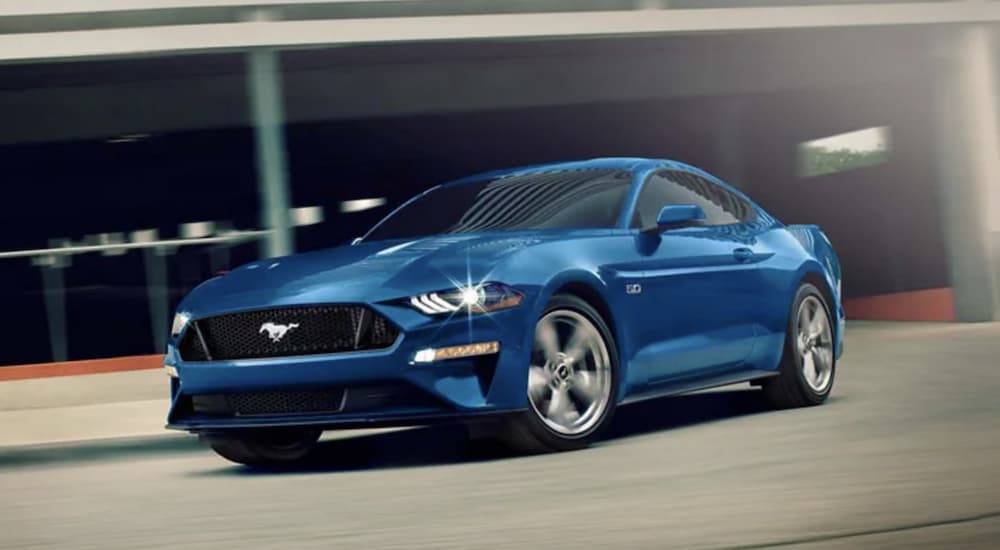 A blue 2022 Ford Mustang GT is shown from the front driving through a parking garage.