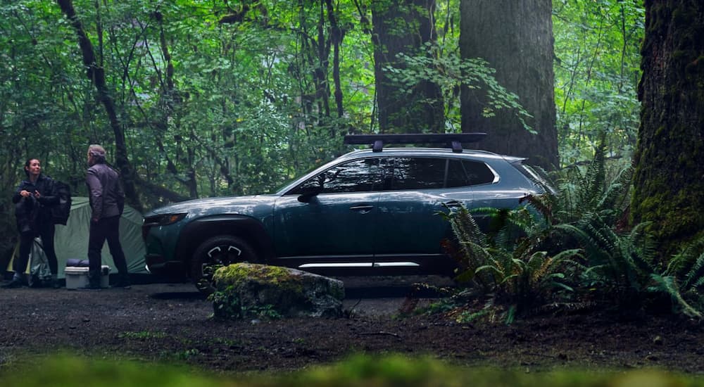 A grey 2023 Mazda CX-50 SUV is shown from the side parked by a hiking trail.