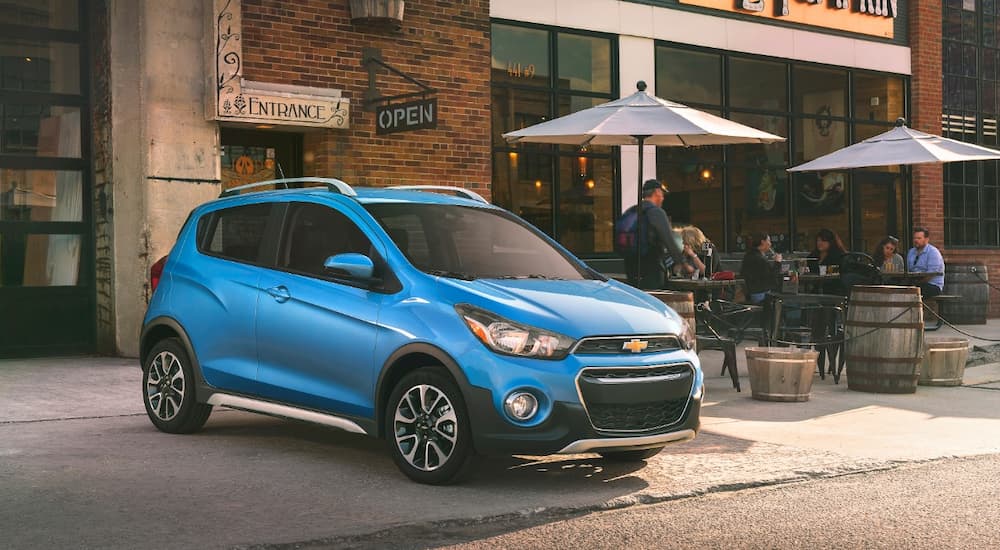 A blue 2019 Chevy Spark is shown parked outside of a cafe.