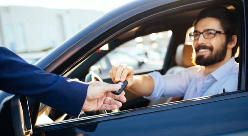 A salesman is shown handing a customer the keys to a used car.