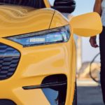A close up shows a person charging a yellow 2021 Ford Mustang Mach-E, one of the most popular used cars on the market.