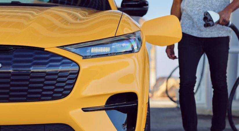 A close up shows a person charging a yellow 2021 Ford Mustang Mach-E, one of the most popular used cars on the market.