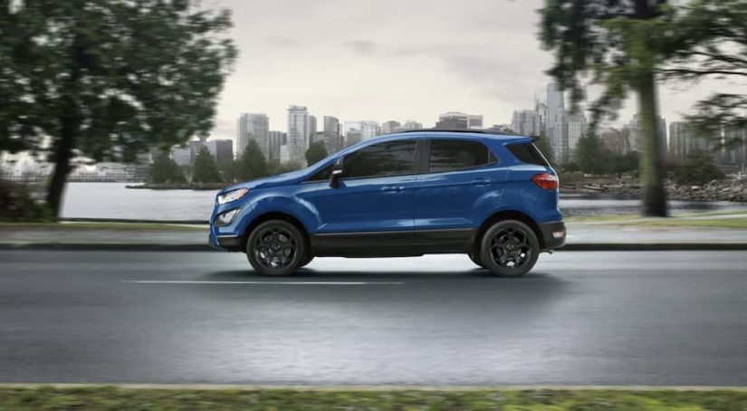 A blue 2021 Ford EcoSport is shown from the side driving on an open road past a city.