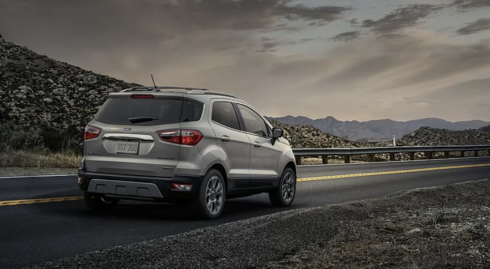 A grey 2021 Ford EcoSport is shown from the rear driving on an open highway in the mountains.